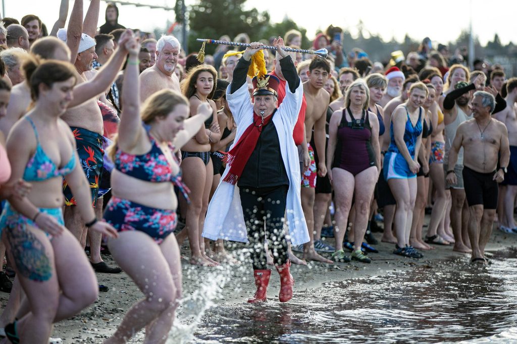Edith Farrar watches as people begin to run into the ocean, perhaps a moment too early, during the 2023 Edmonds Polar Bear Plunge on Sunday, Jan. 1, 2023, at Brackett's Landing in Edmonds, Washington. The sea water was a chilly 47.7 degrees Fahrenheit on New Year's Day. (Ryan Berry / The Herald)