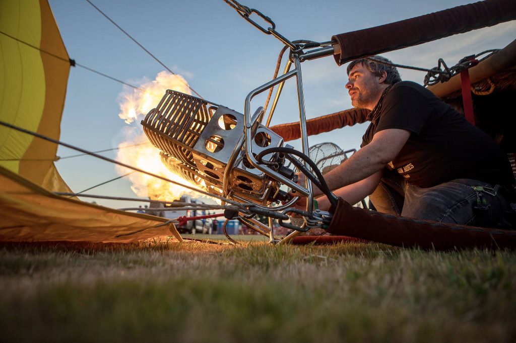 Erin Romaneschi, 33, fires up the burner and injects a hot air balloon with flame to heat the air inside during Kla Ha Ya Days at Harvey Field on Friday, July 14, 2023, in Snohomish, Washington. (Annie Barker / The Herald)