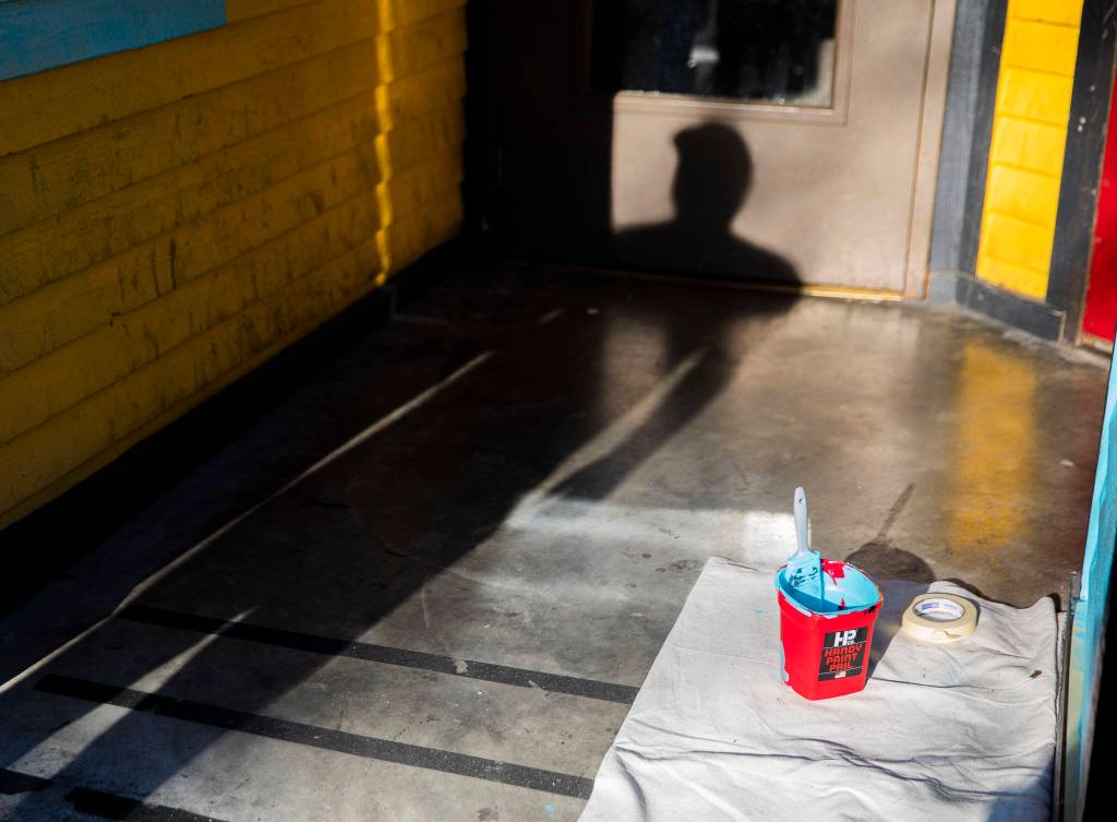 Reed casts a shadow int he entry to the Catalyst Cafe while painting the exterior on Thursday, Dec. 21, 2023 in Everett, Washington. (Olivia Vanni / The Herald)