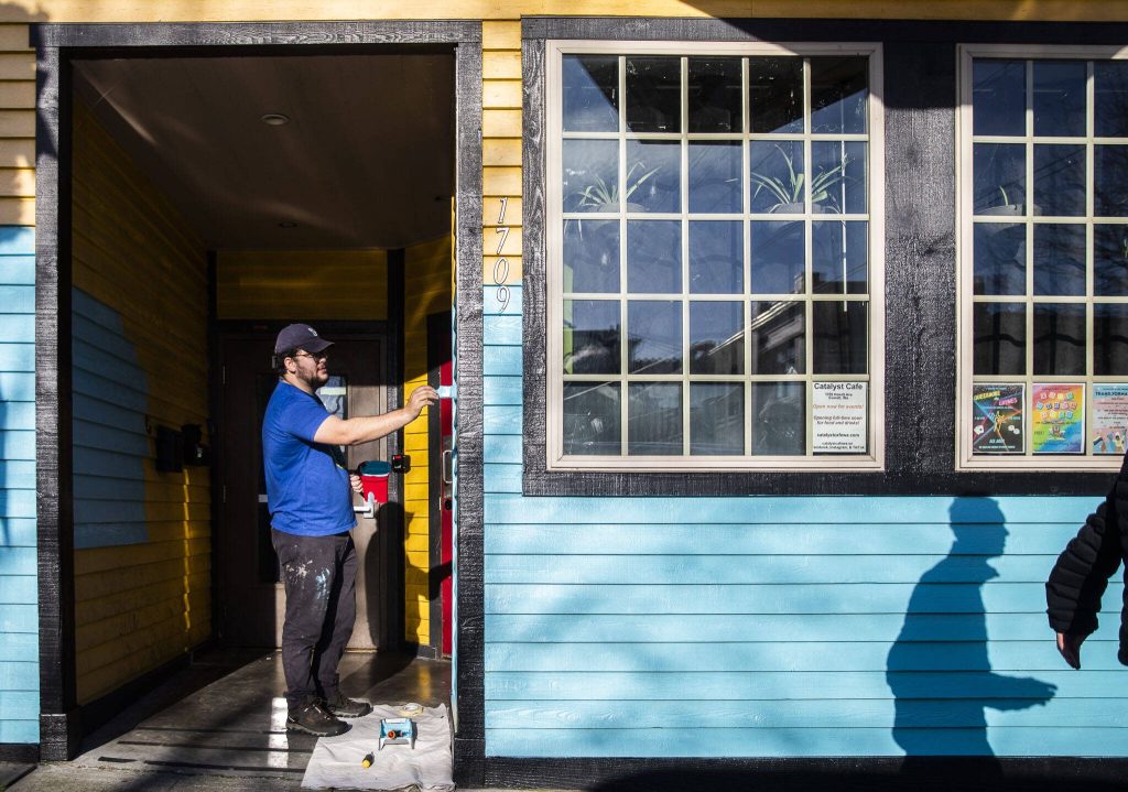 People walk past Evan Reed while repaints the exterior of the Catalyst Cafe on Thursday, Dec. 21, 2023 in Everett, Washington. (Olivia Vanni / The Herald)