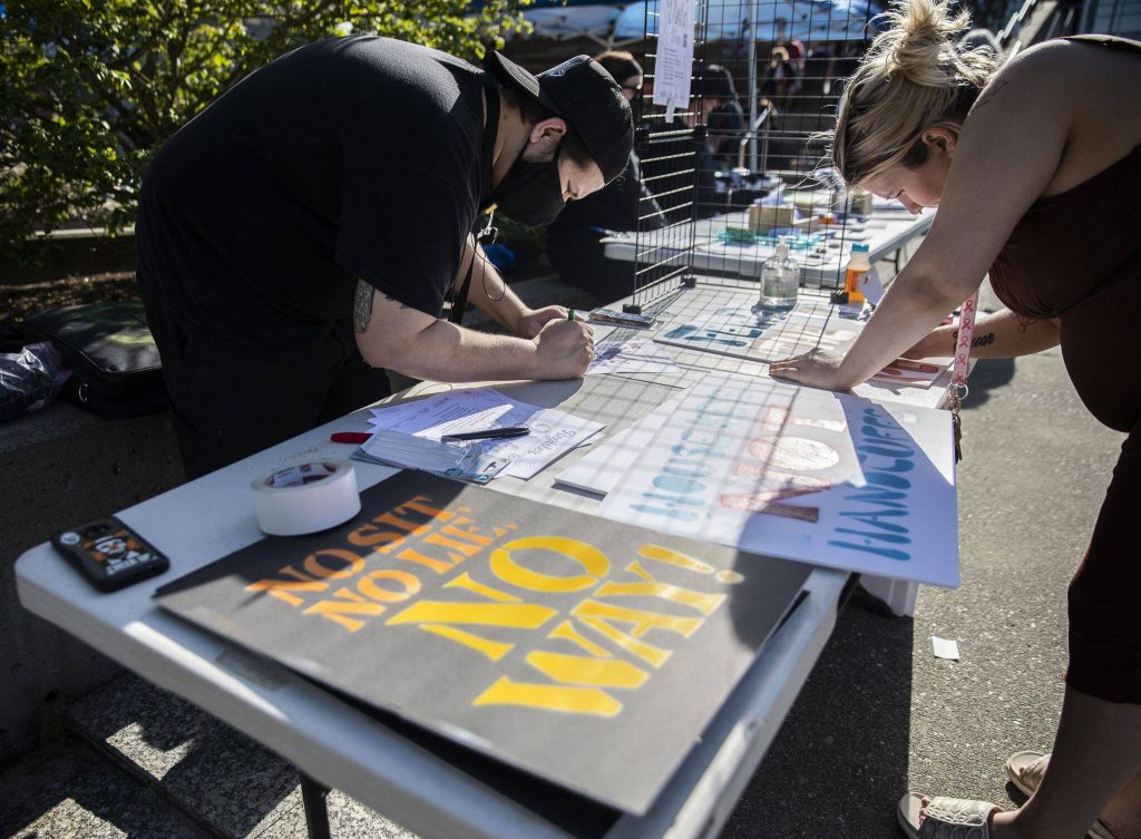 Ruben Trujillo, left and Sarah Bates, right, work on signs in protest of the ���no sit, no lie��� expansion on Wednesday, May 3, 2023 in Everett, Washington. (Olivia Vanni / The Herald)