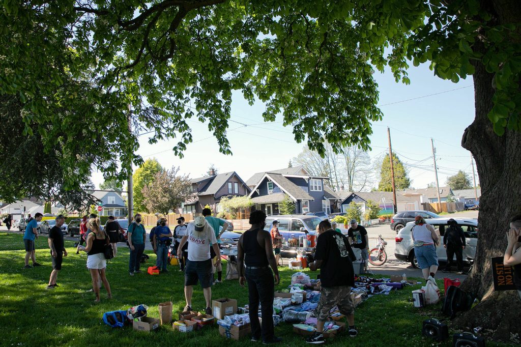 People gather in the shade during a community gathering to distribute food and resources in protest of Everetts expanded no sit, no lie ordinance Sunday, May 14, 2023, at Clark Park in Everett, Washington. (Ryan Berry / The Herald)