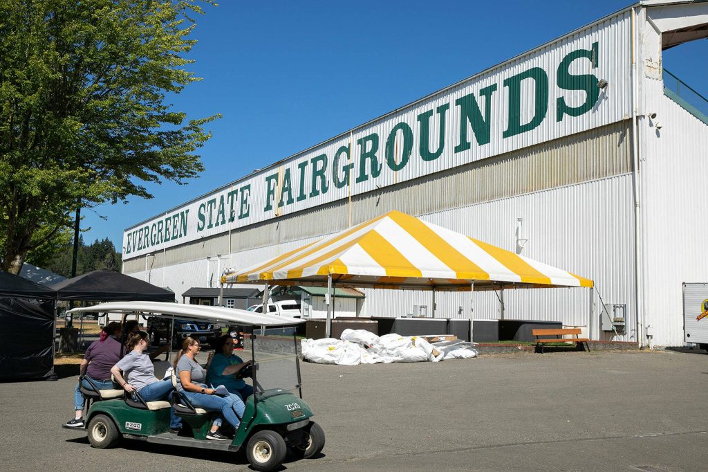 People zip around the fairgrounds on a golf cart as preparations for the state fair are underway on Monday, Aug. 22, 2022, at the Evergreen State Fairgrounds in Monroe, Washington. (Ryan Berry / The Herald)