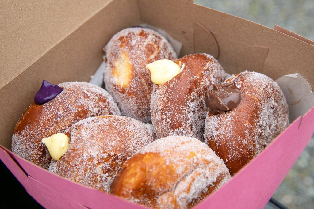 Lori Johnson, director of the Washington State Food Truck Association shows off a box of fresh malasadas during the grand opening of the GoodBelly LLC food truck on Saturday, Jan. 28, 2023, in Everett, Washington. (Ryan Berry / The Herald)
