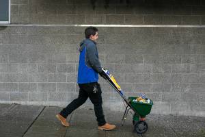 Ryan Whittaker from Skotdal Real Estate lays down ice melt in front of a Hoyt Avenue apartment complex before the arrival of an evening snowfall Thursday, Jan. 11, 2024, in downtown Everett, Washington. (Ryan Berry / The Herald)