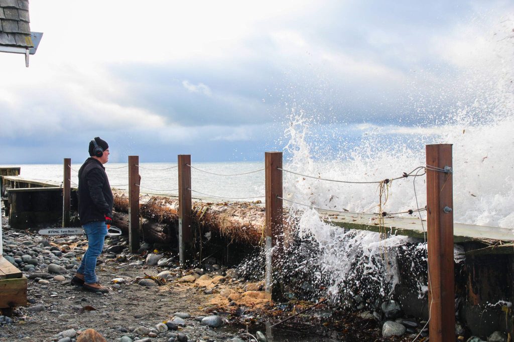Marie Francos husband, Lenny, avoids the splash while taking a short break from cutting a log brought by Tuesdays storm. (Luisa Loi / Whidbey News Times)