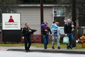 An officer escorts three parents with their children away from KinderCare after a shooting across the street at the Bluffs at Evergreen apartment complex Monday, Jan. 22, 2024, in Everett, Washington. Parents were able to get their children from the daycare center during the standoff. (Ryan Berry / The Herald)