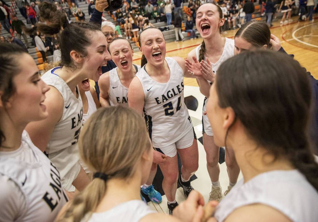 Arlington twins Rachel Snow (center left) and Katie Snow (24) yell in celebration with teammates after winning the Class 3A District 1 championship Feb. 18, 2023 in Everett. (Olivia Vanni / The Herald)