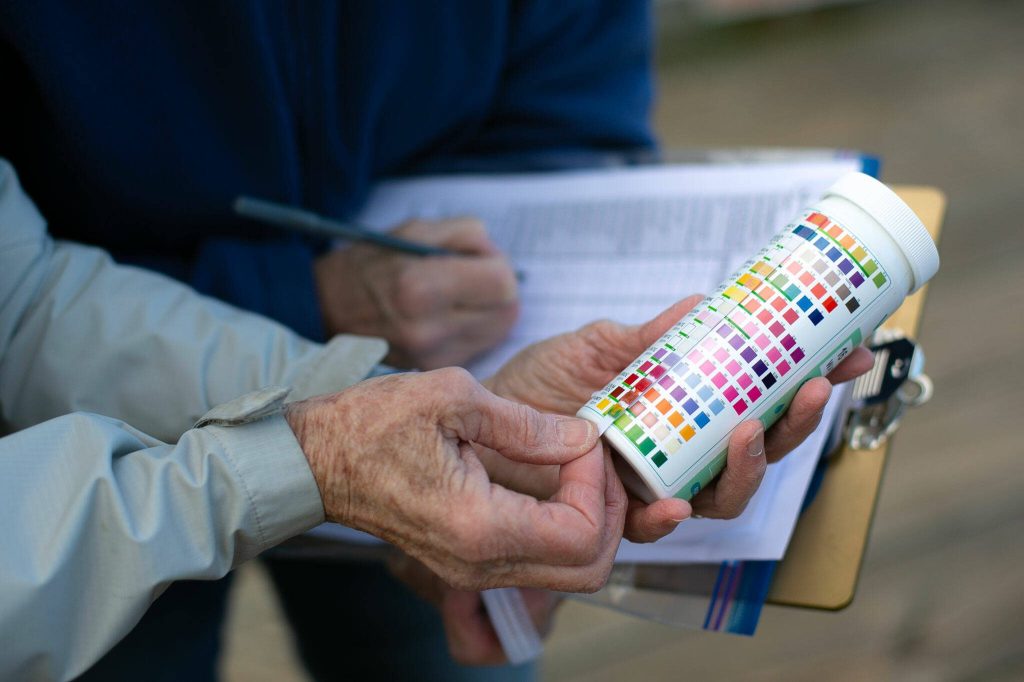 Lynn Lichtenberg and Claudia Douglass read a chemical test strip that is used to measure pollutants in water while conducting stormwater monitoring at the Port of Everett waterfront Friday, Feb. 16, 2024, in Everett, Washington. (Ryan Berry / The Herald)
