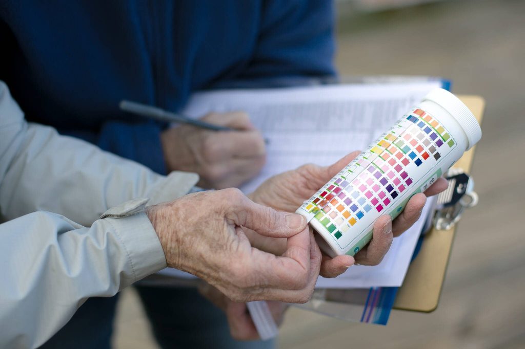 Lynn Lichtenberg and Claudia Douglass read a chemical test strip that is used to measure pollutants in water while conducting stormwater monitoring at the Port of Everett waterfront Friday, Feb. 16, 2024, in Everett, Washington. (Ryan Berry / The Herald)