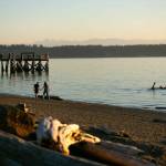People fish from the pier, hold hands on the beach and steer a swamped canoe in the water as the sun sets on another day at Kayak Point on Monday, June 12, 2023, in Stanwood, Washington. (Ryan Berry / The Herald)