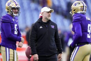 Washington offensive coordinator Ryan Grubb, center, talks with quarterback Dylan Morris (5) and quarterback Michael Penix Jr. (9) as they warm up before an NCAA college football game against Washington State, Saturday, Nov. 25, 2023, in Seattle. (AP Photo/Lindsey Wasson)