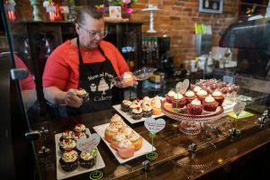 Mom and Pops Cakery owner Colleen Dunn picks out a Valentine’s Day themed cupcake for a customer on Wednesday, Feb. 14, 2024 in Everett, Washington. (Olivia Vanni / The Herald)