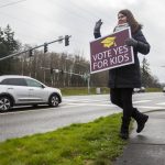 Jaime Benedict, who works as a substitute teacher, waves to drivers on the corner of Mukilteo Speedway and Harbor Pointe Boulevard while holding a sign in support of a bond proposal for Mukilteo School District in February 2020 in Mukilteo. (Olivia Vanni / The Herald file photo)