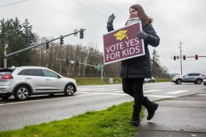 Jaime Benedict, who works as a substitute teacher, waves to drivers on the corner of Mukilteo Speedway and Harbor Pointe Boulevard while holding a sign in support of the $240 million capital bond proposal for Mukilteo School District on Tuesday, Feb. 11, 2020 in Mukilteo, Wash. (Olivia Vanni / The Herald)