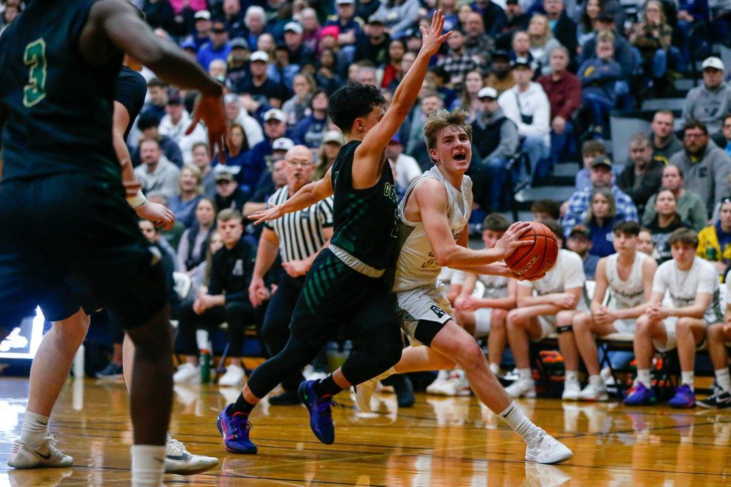 Arlington junior guard Leyton Martin drives on Marysville Getchells Bubba Palocol during a playoff matchup at Arlington High School on Saturday, Feb. 24, 2024, in Arlington, Washington. (Ryan Berry / The Herald)