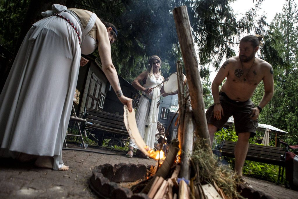 NMier LaVeau, left, and Jesse Sterland, right, start a fire for the Lammas and Wicker Man ritual while Mydnyte Windham, center, drums at the Aquarian Tabernacle Church in Index, Washington, in August 2023. (Annie Barker / The Herald)