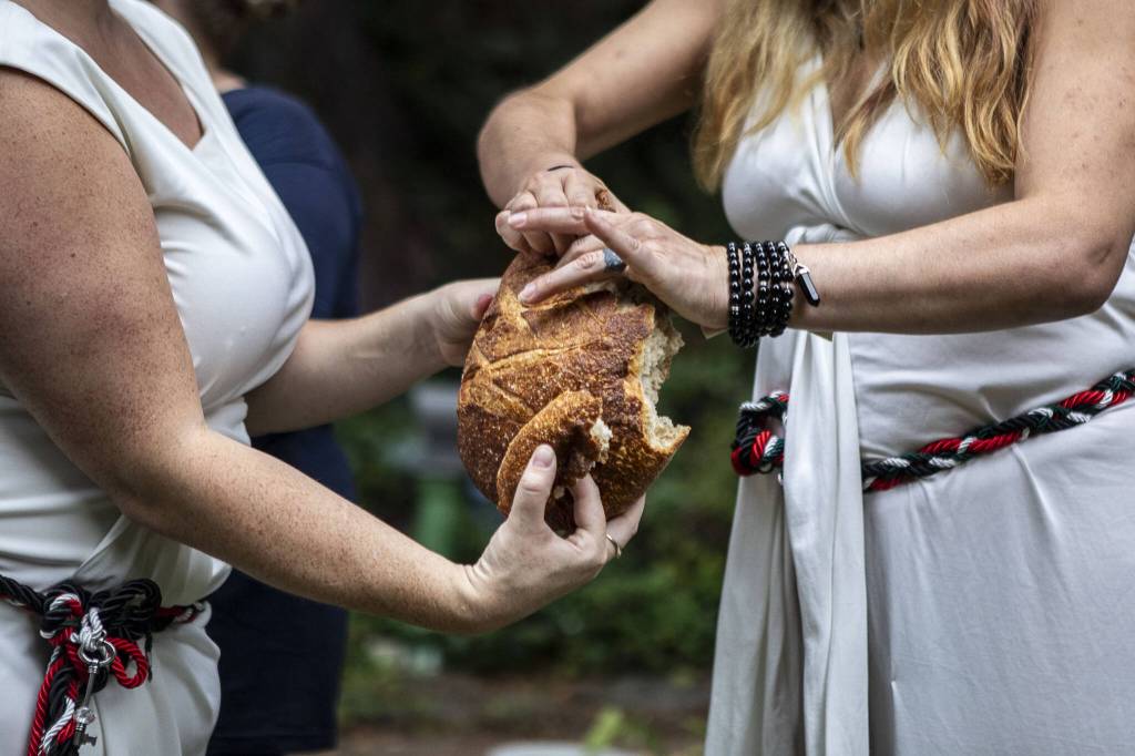 Pagans from around Puget Sound break bread during the Lammas and Wicker Man ritual at the Aquarian Tabernacle Church in Index, Washington, on Aug. 5, 2023. According to the church, the bread signifies an abundant harvest, and that the gods will ensure their needs are provided for if each person does their part for the group. (Annie Barker / The Herald)