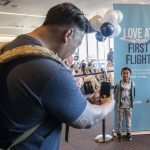 Ron Rendorio, left, takes a photo of Kamron, 6, in front of a sign announcing Alaskas first flight to Honolulu from Paine Field on Nov. 17, 2023 in Everett. (Olivia Vanni / The Herald)