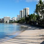 A man sits on a nearly empty Waikiki Beach in Honolulu, Friday, Oct. 2, 2020. (AP Photo/Caleb Jones, file)