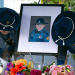 Two troopers place a photo of their slain colleague, Chris Gadd, outside state patrols District 7 Headquarters about twelve hours after Gadd was struck and killed on southbound I-5 about a mile from the headquarters on Saturday, March 2, 2024, in Marysville, Washington. (Ryan Berry / The Herald)
