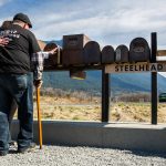 Ron Thompson, right, embraces his wife Gail Thompson, left, as she reaches out to touch a replica of their mailbox during the Oso slide remembrance ceremony on Friday, March 22, 2019 in Oso, Washington. (Olivia Vanni / The Herald)