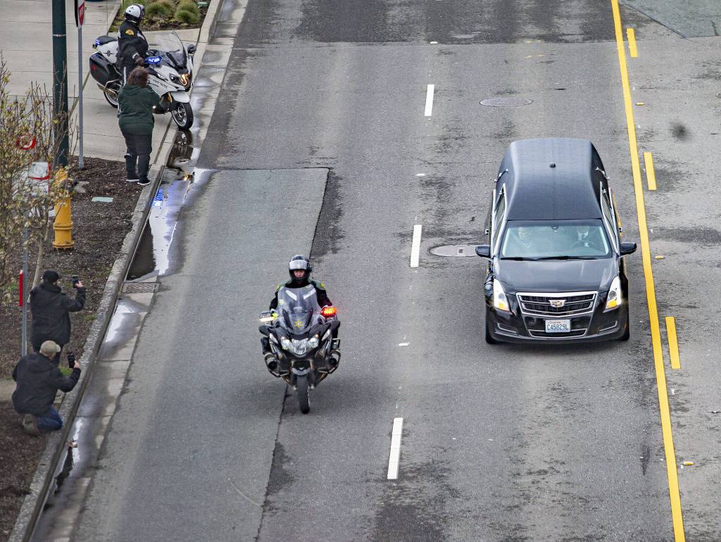 People stand along Marine View Drive and watch the hearse carrying Washington State trooper Christopher Gadds remains in a memorial procession on Tuesday, March 12, 2024, in Everett, Washington. (Olivia Vanni / The Herald)