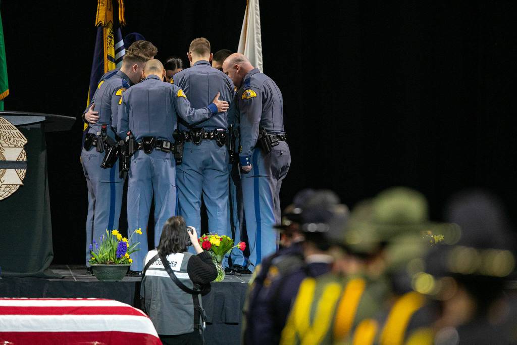A group of Washington State Patrol trooper Chris Gadds closest friends and coworkers add a ribbon baring his name to the Washington State Patrol flag on Tuesday, March 12, 2024, at Angel of the Winds Arena in Everett, Washington. (Ryan Berry / The Herald)
