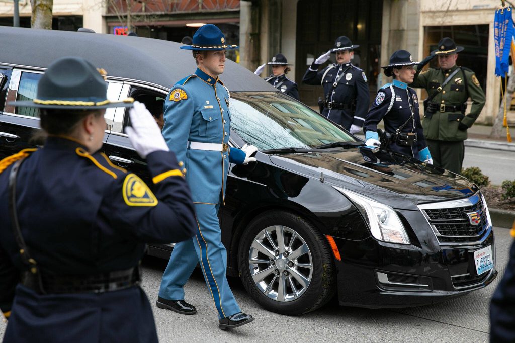 A hearse carrying Washington State Patrol trooper Chris Gadds remains arrives at Angel of the Winds Arena on Tuesday, March 12, 2024, in Everett, Washington. (Ryan Berry / The Herald)
People stand along Marine View Drive and watch the hearse carrying Washington State Patrol trooper Christopher Gadds remains in a memorial procession on Tuesday, March 12, 2024, in Everett, Washington. (Olivia Vanni / The Herald)