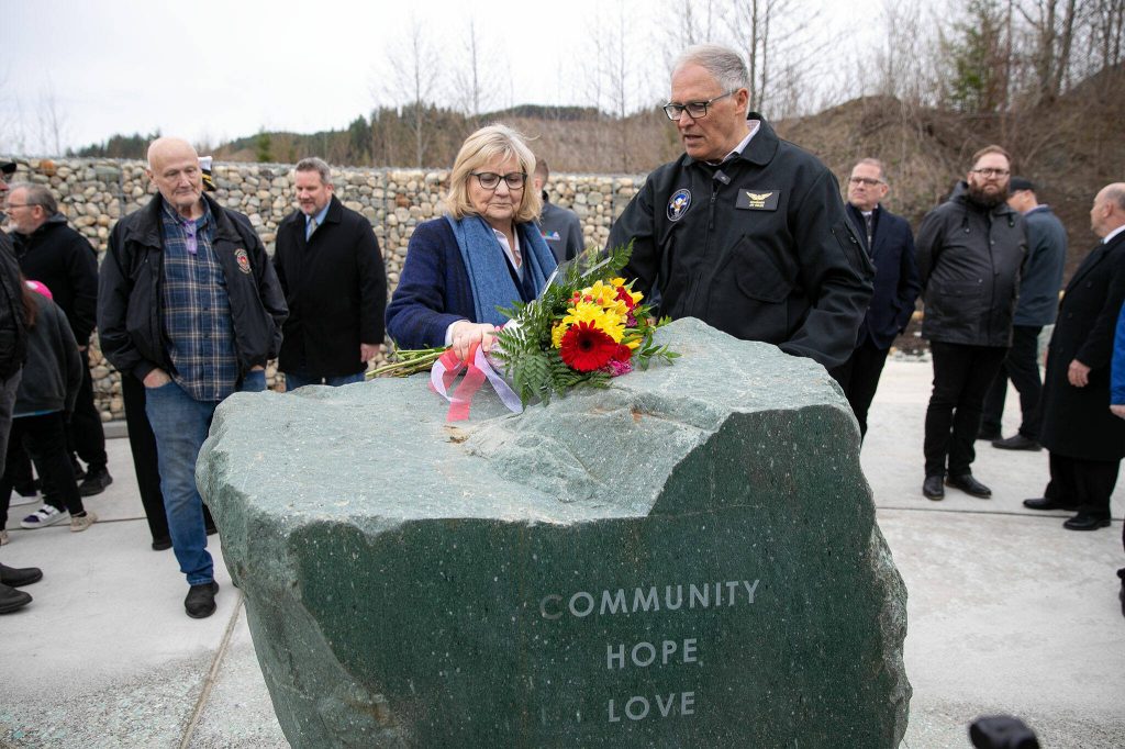 Gov. Jay Inslee and wife Trudi lay a bouquet of flowers at the Oso Landslide Memorial during the ten-year remembrance of the Oso landslide on Friday, March 22, 2024, in Oso, Washington. (Ryan Berry / The Herald)