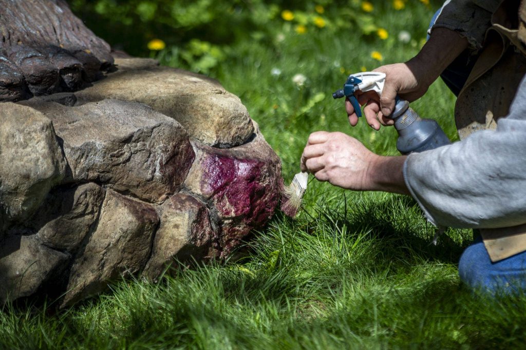Terry Carrigan, 60, adds touches to the base of a giant Bigfoot he made at his home-based Skywater Studios on Sunday, April 14, 2024 in Monroe, Washington. (Annie Barker / The Herald)