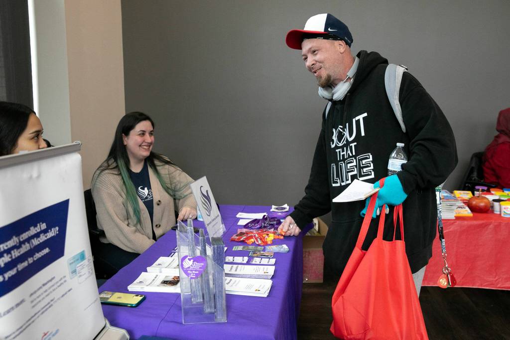 Chad Hughes speaks with a couple booth attendants during a resource fair at the Carnegie Resource Center on Wednesday, March 6, 2024, in downtown Everett, Washington. (Ryan Berry / The Herald)