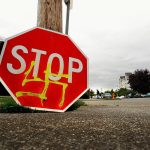 A stop sign defaced with a spray-painted swastika sits on the ground at the corner of 25th Street and Rucker Avenue while a City of Everett worker installs a new sign in the summer of 2009. (Dan Bates / Herald file photo)