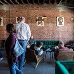 People make themselves at home at the front of Obsidian Beer Hall on Friday, April 12, 2024, in downtown Everett, Washington. Art by Jessie Lipscomb or Momma Lips Draws hangs on the wall behind them.