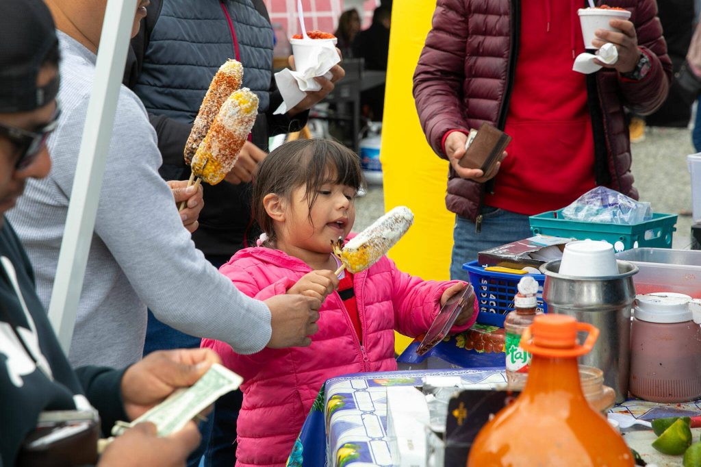 A young girl takes her elote from Seattle Sweecorn at the Hidden Gems Weekend Market on Sunday, April 28, 2024, at Boom City in Tulalip, Washington. (Ryan Berry / The Herald)