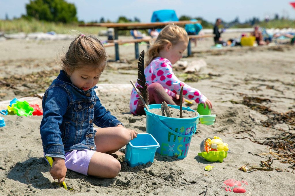 Annie Meadows and Penelope Anderson, both 3, make sandcastles at the Jetty Island beach while visiting with their mothers and siblings on Friday, July 7, 2023, in Everett, Washington. (Ryan Berry / The Herald)