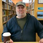 George Beard takes a seat at his spot inside the Stanwood Library on Thursday, May 23, 2024, in Stanwood, Washington. The space is free to use and enables Beard to search for housing online and keep up on his paperwork as he seeks shelter and financial support. (Ryan Berry / The Herald)