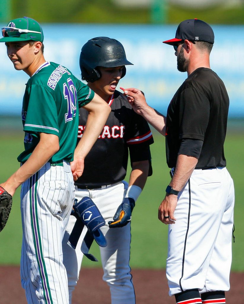 Mountlake Terraces Talan Zenk receives a gummy worm from his first base coach after reaching safely against Edmonds-Woodway in the Class 3A District 1 baseball championship Saturday, May 11, 2024, at Funko Field in Everett, Washington. (Ryan Berry / The Herald)