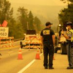 State Trooper Isaiah Oliver speaks to a BNSF worker at mile marker 31.7 as road closures and evacuations mount in response to the Bolt Creek Fire on Saturday, Sep. 10, 2022, on U.S. 2 near Index, Washington. (Ryan Berry / The Herald)