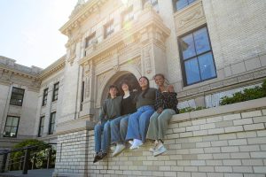 Everett High seniors, from left, Avery Thompson, Lanie Thompson, Melissa Rosales-Alfaro and Saron Mulugeta sit together in front of their school on Monday, May 20, 2024, in Everett, Washington. The group have called to question their district’s policy that does not permit graduates to decorate their mortarboards or graduation clothing. (Ryan Berry / The Herald)