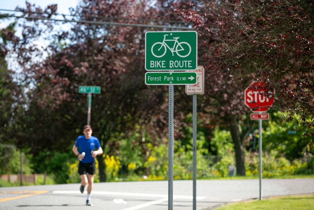 A runner crosses Federal Avenue near 46th Street SE by a bike wayfinding sign on Thursday, May 23, 2024, in Everett, Washington. (Ryan Berry / The Herald)