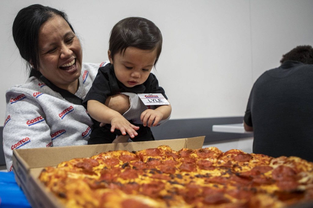 Family friend Nian Enriquez, left, smiles as Carlisle Lyle Sarmiento, right, reaches for a pizza during his first birthday party at Costco in Lake Stevens on Friday, May 31, 2024. (Annie Barker / The Herald)