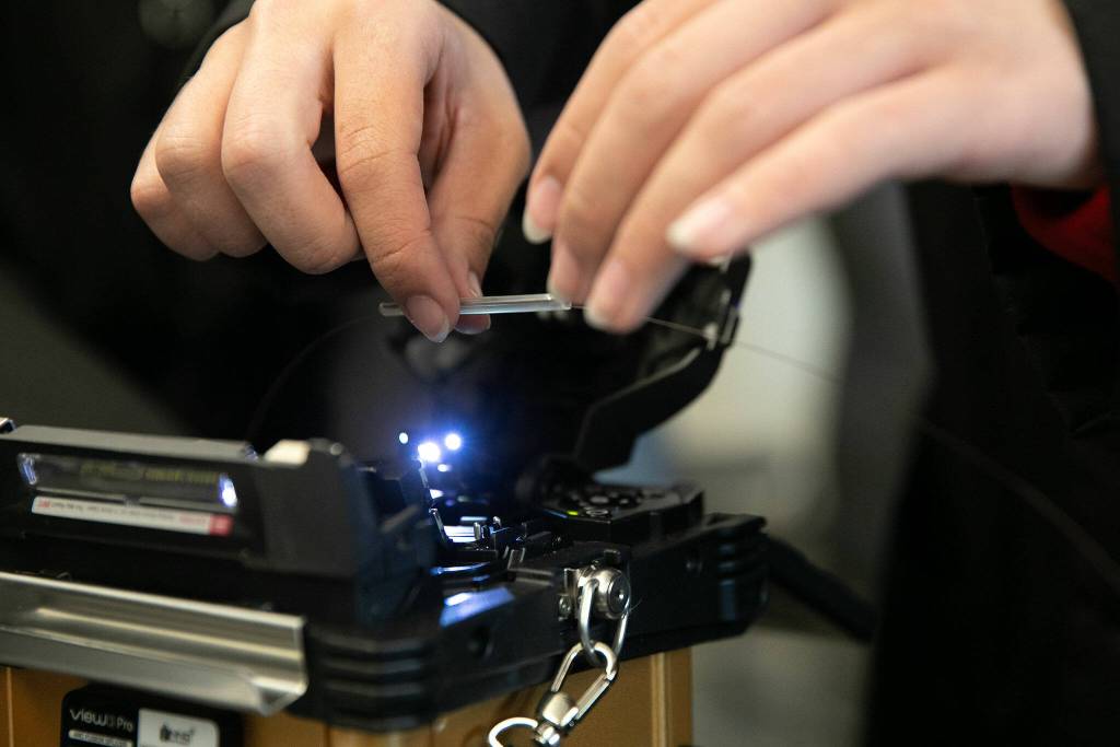 Senior Nano Portugal places a segment of heat shrink tubing into a fusion splicer during a fiber optic technician training demonstration at Sno-Isle TECH Skills Center on Tuesday, May 28, 2024, in Everett, Washington. (Ryan Berry / The Herald)