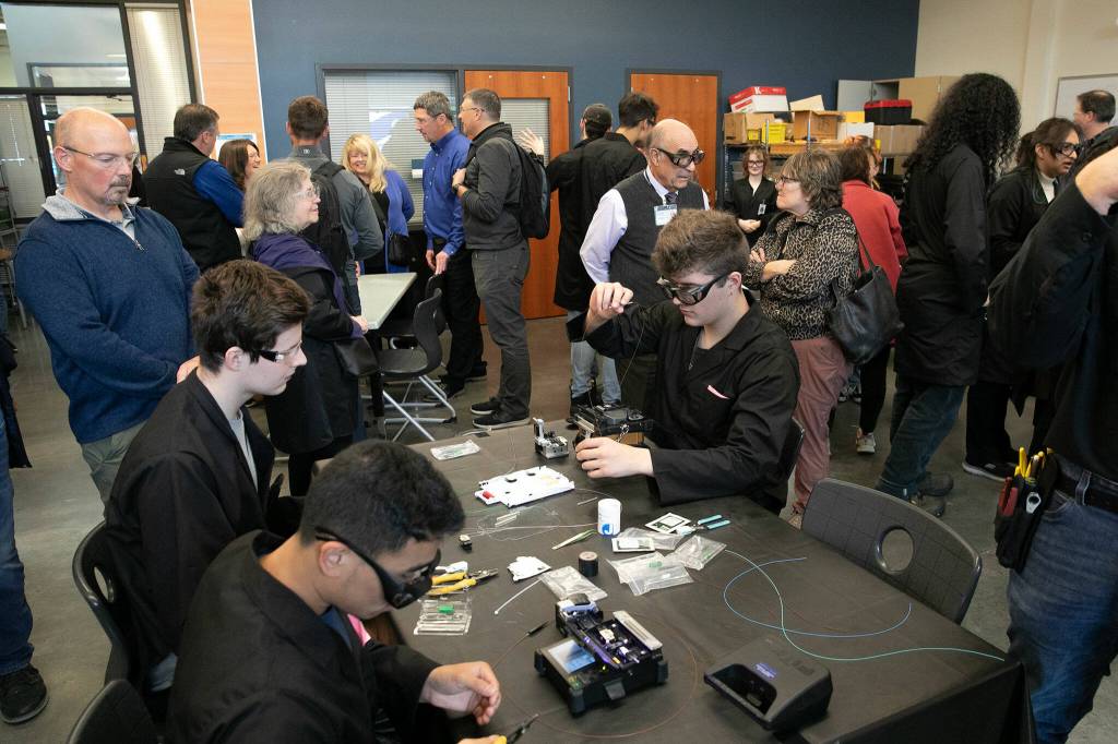 Visitors go from table to table and speak with students during a fiber optic technician training demonstration at Sno-Isle TECH Skills Center on Tuesday, May 28, 2024, in Everett, Washington. (Ryan Berry / The Herald)