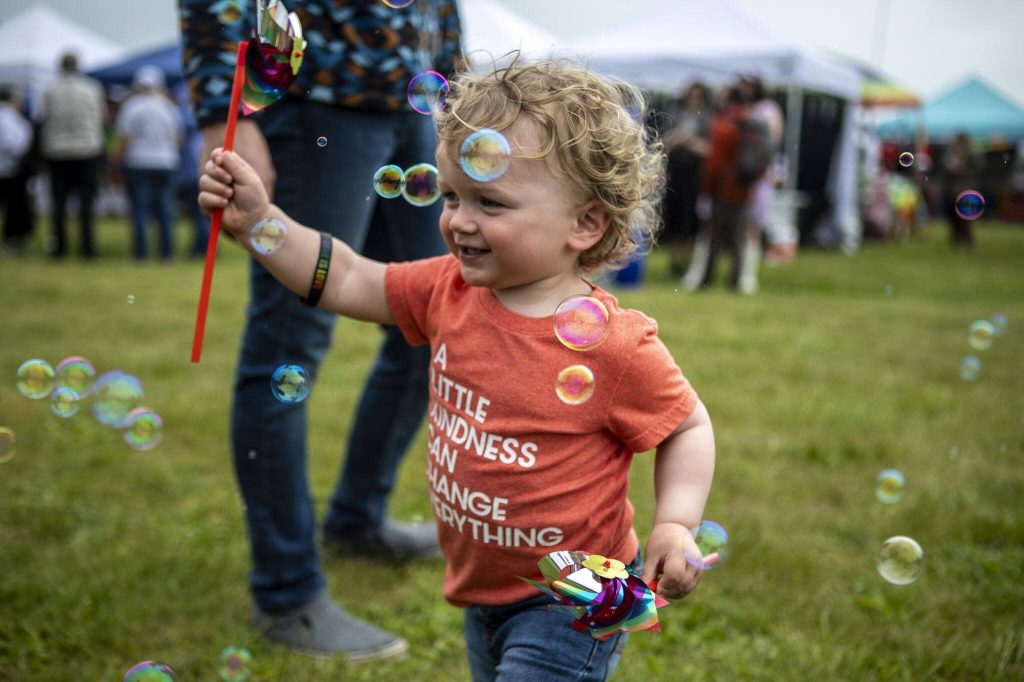 Graham Cox, 1, runs with pinwheels amongst bubbles during the Stanwood-Camano Pride event at Freedom Park in Camano, Washington on Saturday, June 1, 2024. (Annie Barker / The Herald)