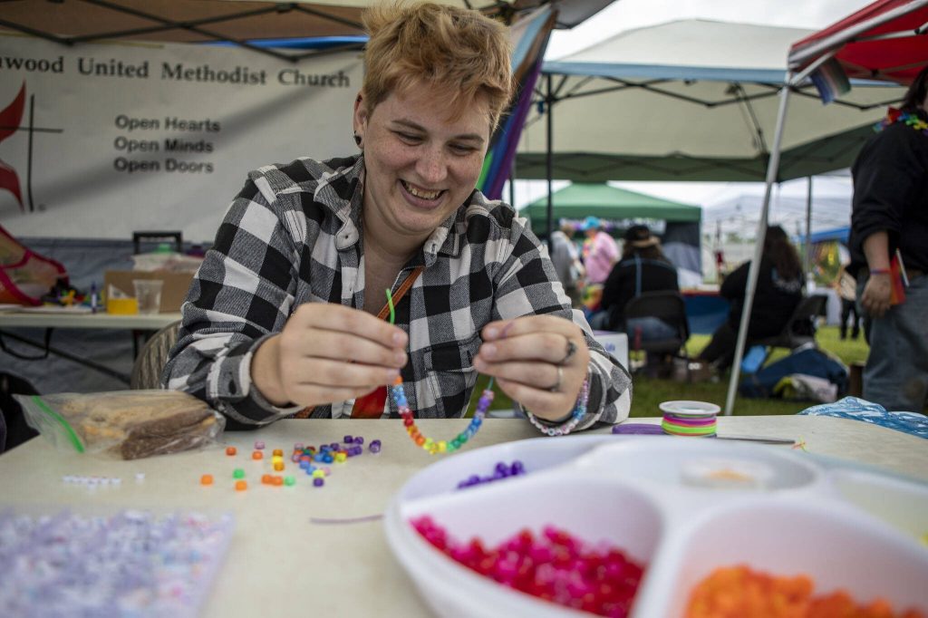 Ashton Fae makes bracelets during the Stanwood-Camano Pride event at Freedom Park in Camano, Washington on Saturday, June 1, 2024. (Annie Barker / The Herald)
