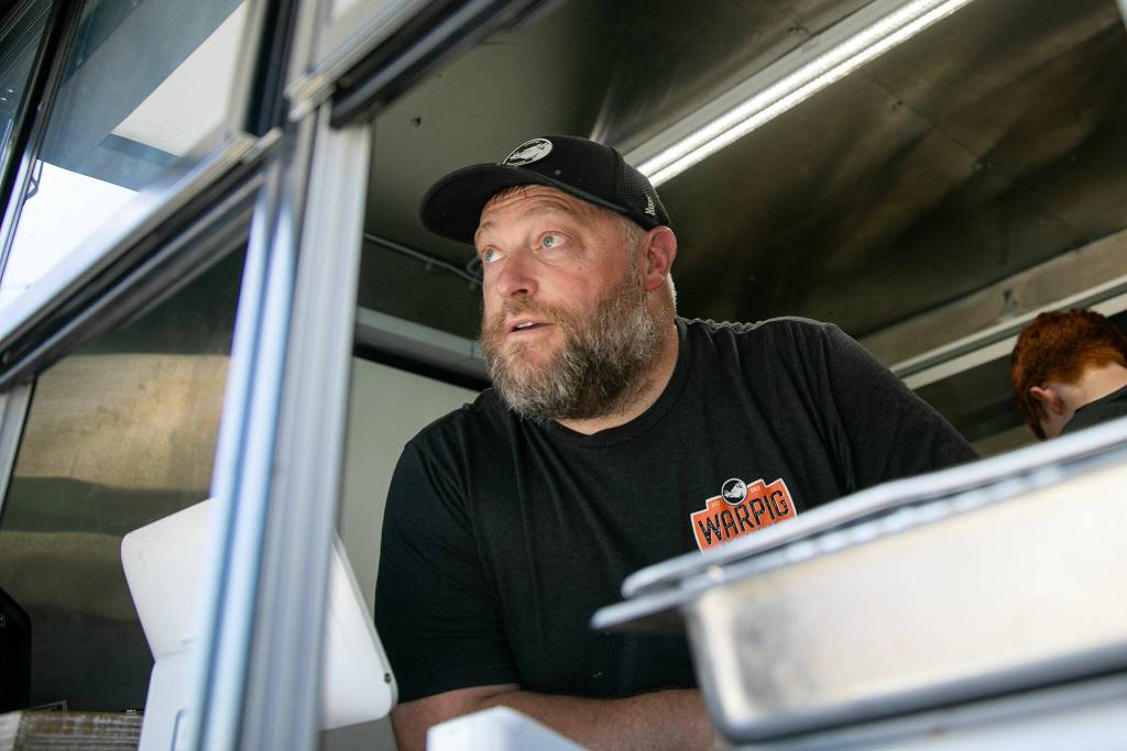 Jason Bauer, of Warpig Smokehouse, chats with some customers while taking orders at the Lake Stevens Farmers Market on Wednesday, June 12, 2024, in Lake Stevens, Washington. (Ryan Berry / The Herald)