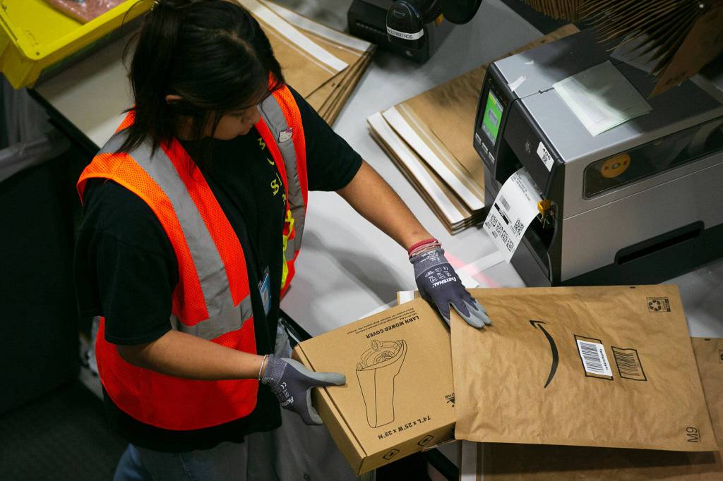An Amazon worker packages a lawnmower cover while processing orders at the new PAE2 Amazon Fulfillment Center on Thursday, Sept. 14, 2023, in Arlington, Washington. (Ryan Berry / The Herald)