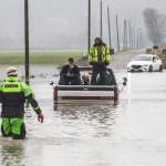 Snohomish County Sheriff Dive Team and Search and Rescue deputy William Dawson approach two men and two dogs sitting in the bed of their truck. The truck died while trying to cross floodwaters along 28th Avenue NW on Wednesday, Dec. 6, 2023, in Stanwood, Washington. (Olivia Vanni / The Herald)