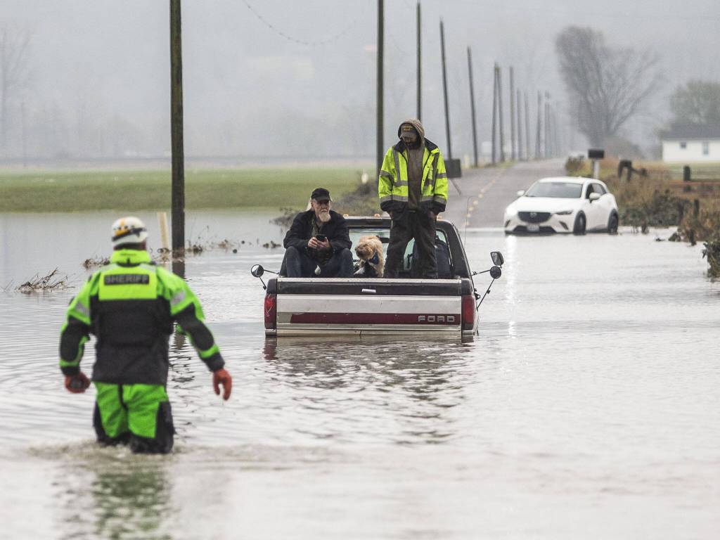 Snohomish County Sheriff Dive Team and Search and Rescue deputy William Dawson approach two men and two dogs sitting in the bed of their truck. The truck died while trying to cross floodwaters along 28th Avenue NW on Wednesday, Dec. 6, 2023, in Stanwood, Washington. (Olivia Vanni / The Herald)